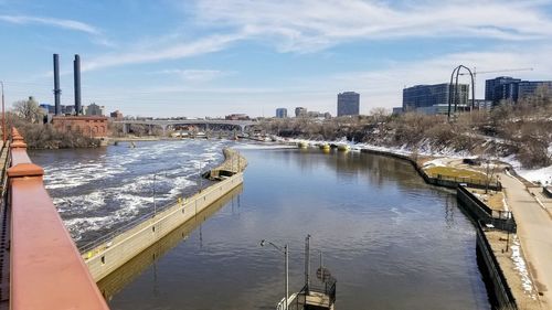 Bridge over river by buildings in city against sky