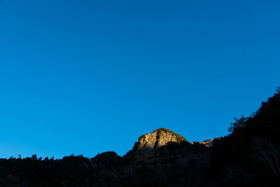 Low angle view of silhouette mountain against clear blue sky