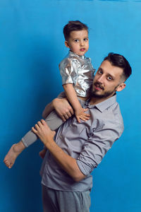 Dad in a shirt with his son standing in the studio on a blue background