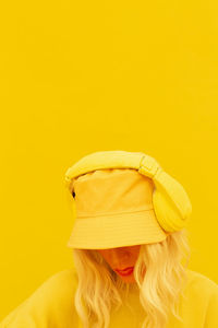 Woman wearing headphones standing against yellow background