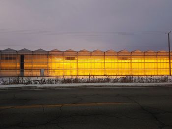 Road by illuminated hydroponic building,  against sky at dusk.