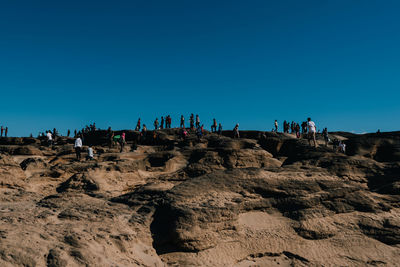Low angle view of people standing on landscape against clear blue sky