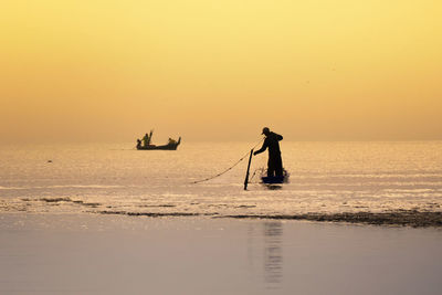 Silhouette man standing on sea against sky during sunset