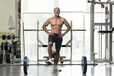 Full length of shirtless man with barbell standing in gym