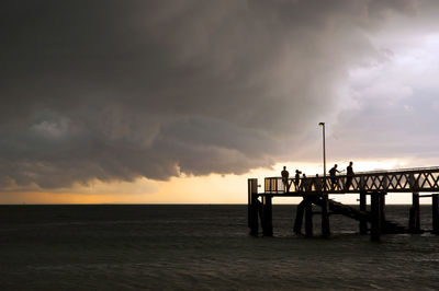 Huge black storm clouds gather as silhouetted people fish off a pier