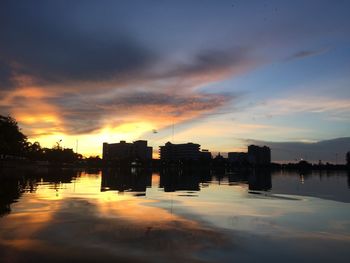 Silhouette buildings by lake against sky during sunset