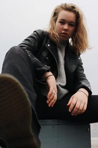 Low angle portrait of beautiful young woman sitting against sky