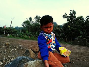 Portrait of boy puckering lips while sitting on rock against sky