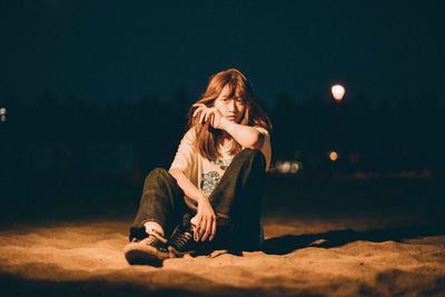 Young woman sitting in illuminated city at night