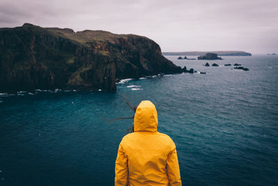 Rear view of woman standing by sea and cliff against sky