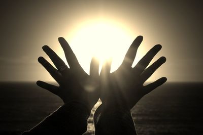 Close-up of silhouette hand against sea during sunset