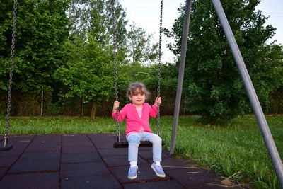 Full length portrait of girl on swing in playground