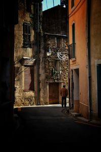 Rear view of man walking on street amidst buildings in city