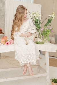 The girl is sitting at the easter table with cakes, spring flowers and quail eggs 