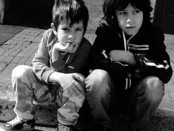 Portrait of boy with thoughtful brother sitting on sidewalk