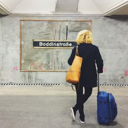 Rear view of woman with luggage waiting on railway station platform