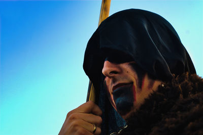 Low angle view of man with face paint wearing costume standing against sky