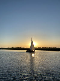 Sailboat in sea against clear sky during sunset