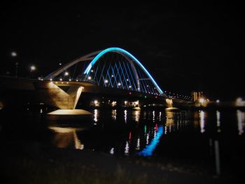 Illuminated ferris wheel by river against sky at night
