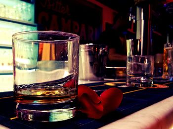 Close-up of scotch whisky in glass with red rose petal on bar counter at nightclub