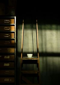 Coffee cup of wooden table by shelf against wall