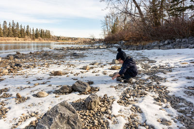 Side view of boy on snow covered field by river 