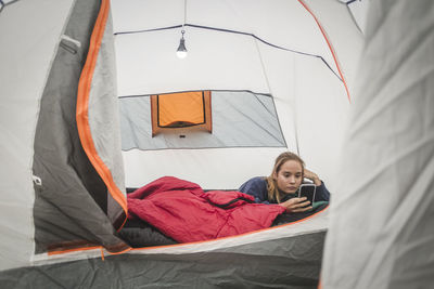 Teenage girl using smart phone while lying in tent