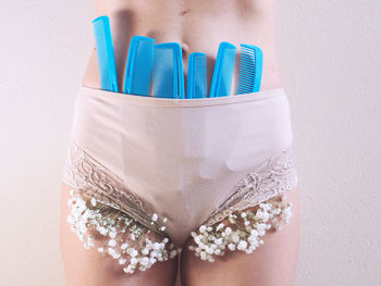 Midsection of woman with combs and flowers in panties against wall