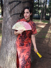 Portrait of smiling young woman standing on tree trunk