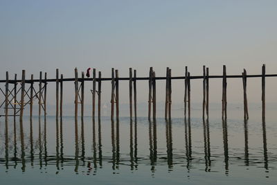 Person walking on footbridge with reflection in sea against sky