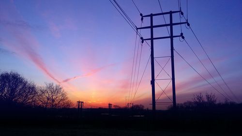 Electricity pylons on landscape at sunset