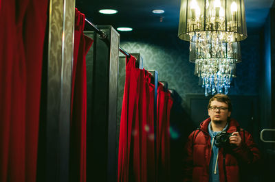 Portrait of man with camera standing in illuminated corridor