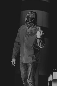 Man wearing skull mask while showing obscene gesture at night