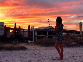 Full length of woman standing at beach against orange sky