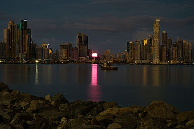 Illuminated buildings by sea against sky at night