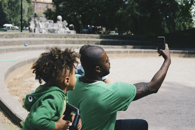 Father taking selfie with children through smart phone while sitting at park