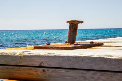 Wooden post on pier by sea against clear sky