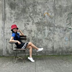 Portrait of young woman sitting on chair against wall