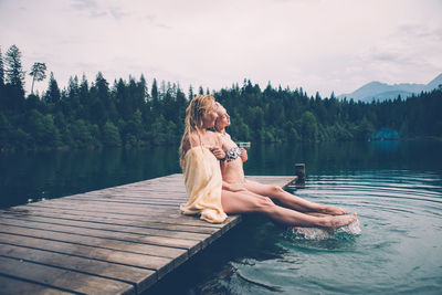 Woman sitting by lake against sky