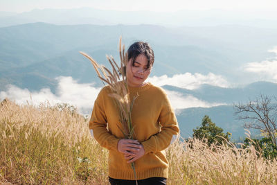 Woman holding plants while standing on mountain