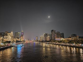 Illuminated buildings by river against sky at night