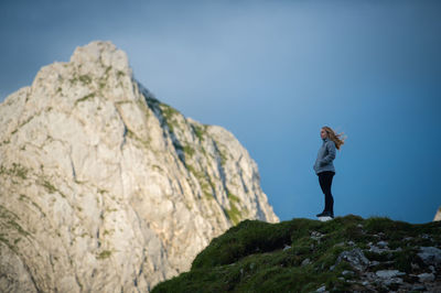 Low angle view of woman standing at mountain against blue sky