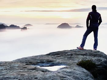 Rear view of man standing on rock against sky