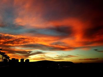 Silhouette buildings against dramatic sky during sunset