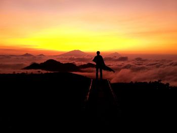 Silhouette man standing on mountain against orange sky