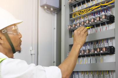 Male electrician working in control panel, electrical maintenance work.