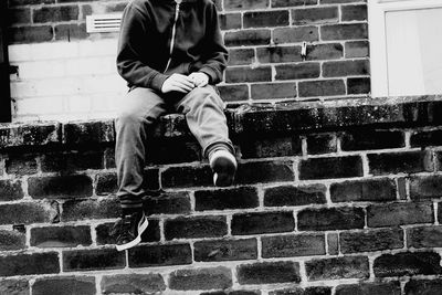 Low section of man sitting on brick wall
