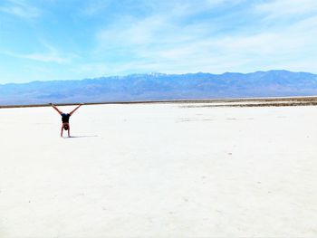 Full length rear view of woman doing cartwheel in desert against sky