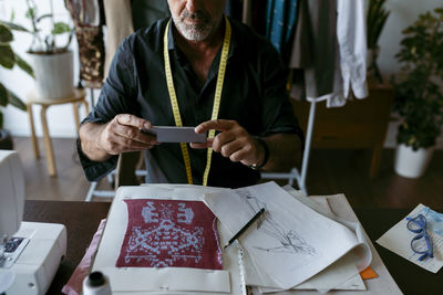 Talented male tailor photographing patterned fabric at work studio