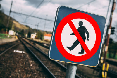 Close-up of warning sign with railroad tracks in background